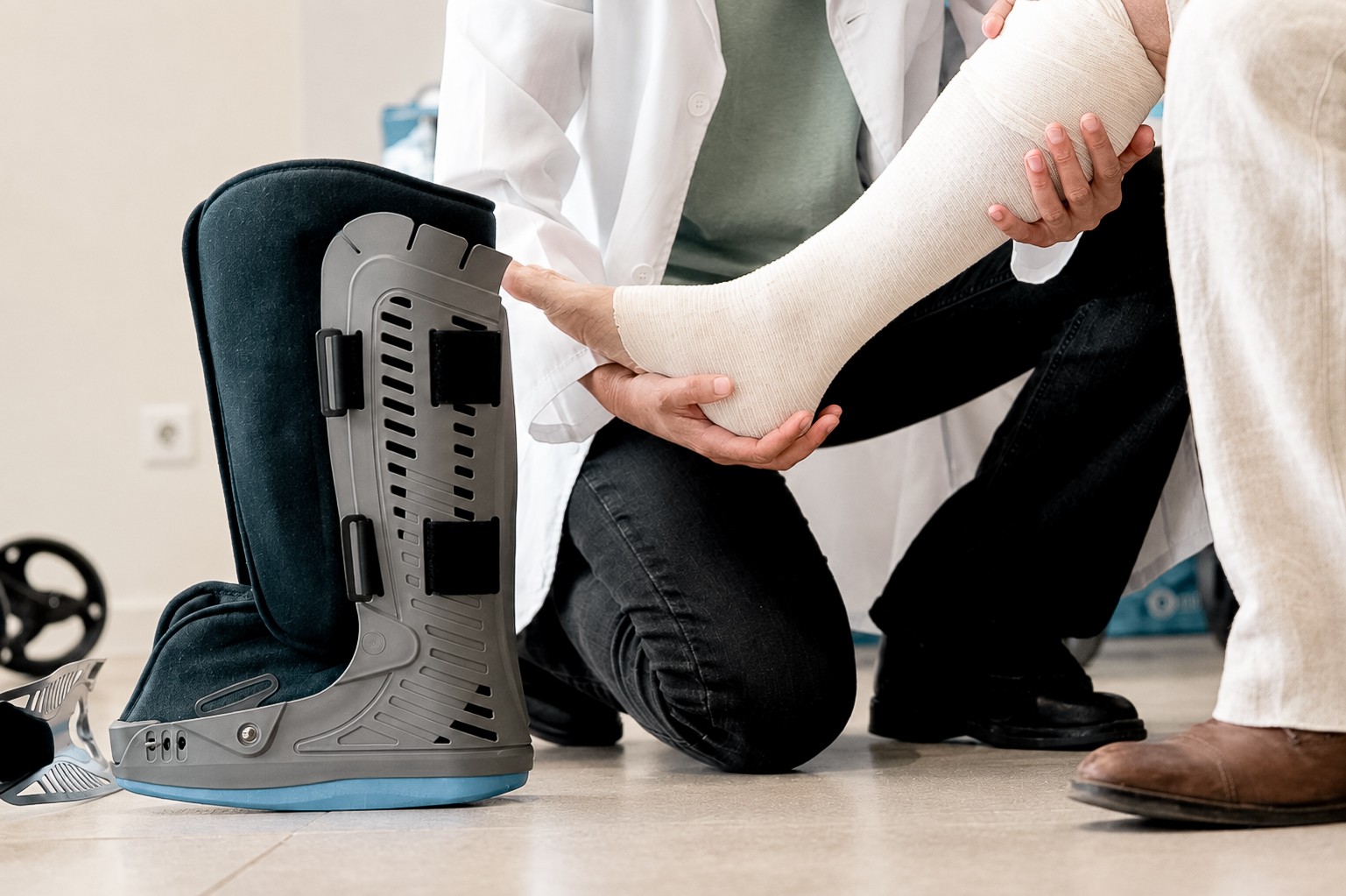A doctor holding a patient’s bandaged foot beside a walking boot (stock photo, posed by models)